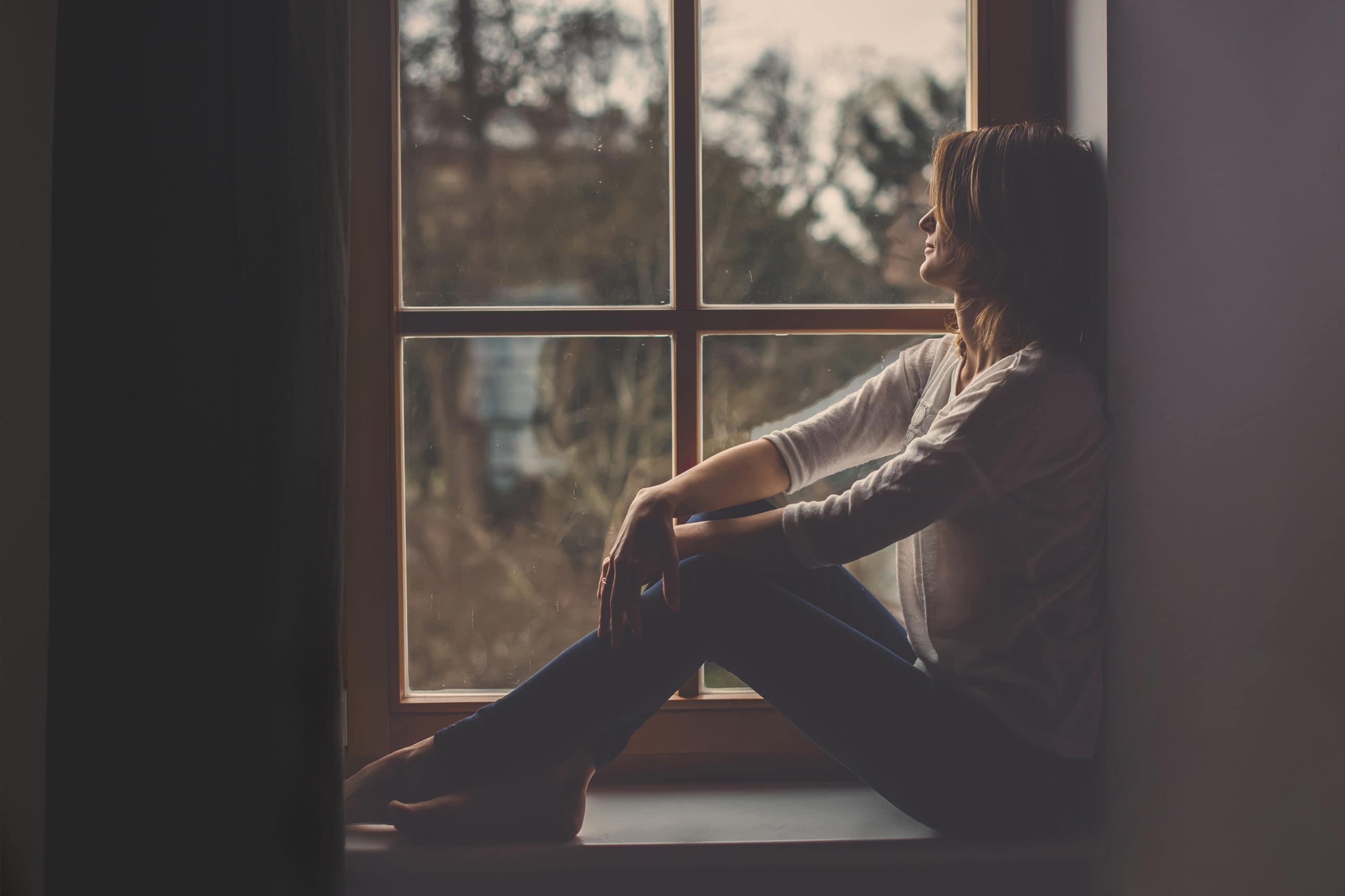Ung kvinne, sitter på et vindu, ser utenfor, ensom humør