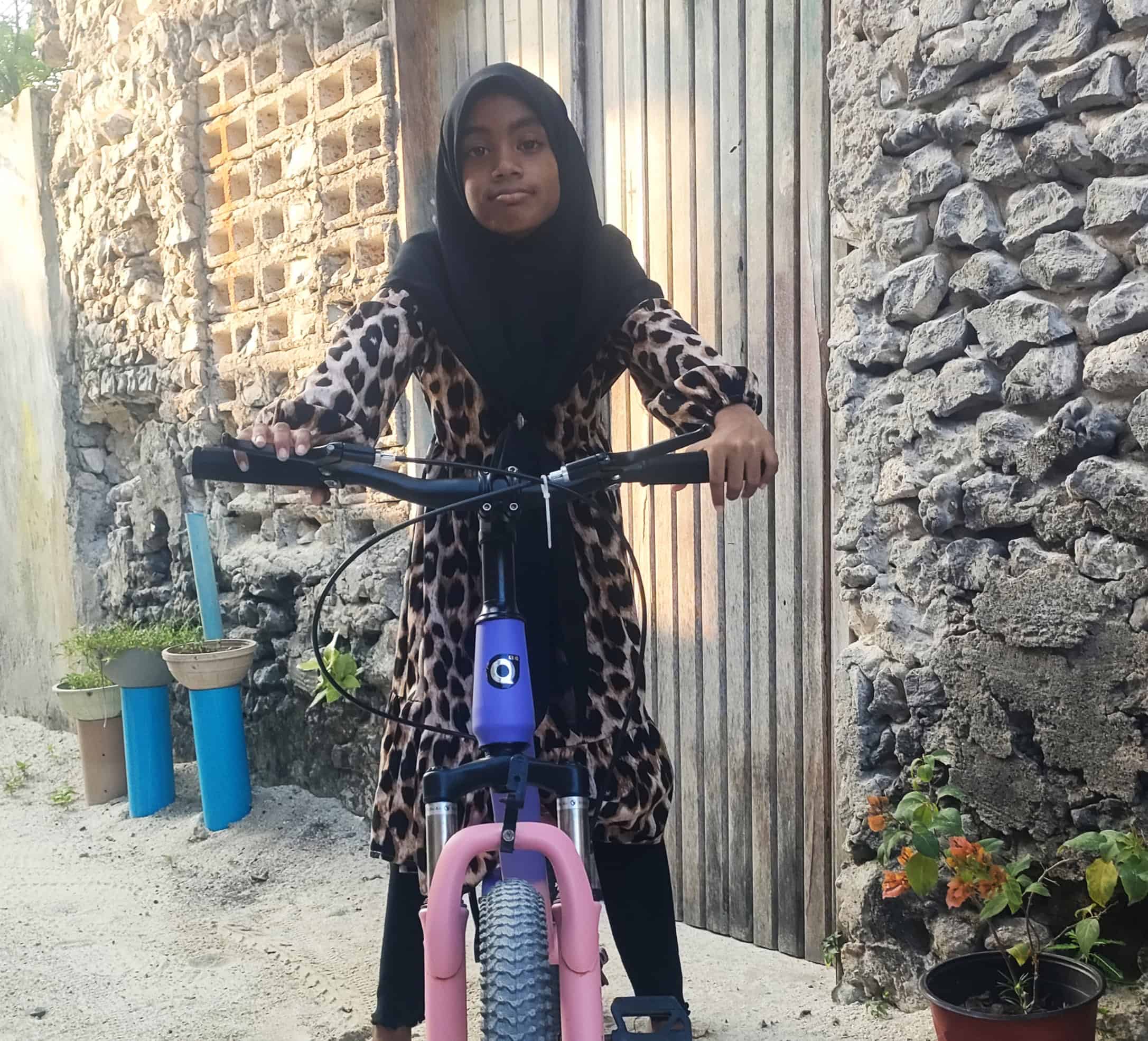 Ti år gamle Rihanna fra Maldivene poserer på en lilla sykkel utenfor et steinhus.