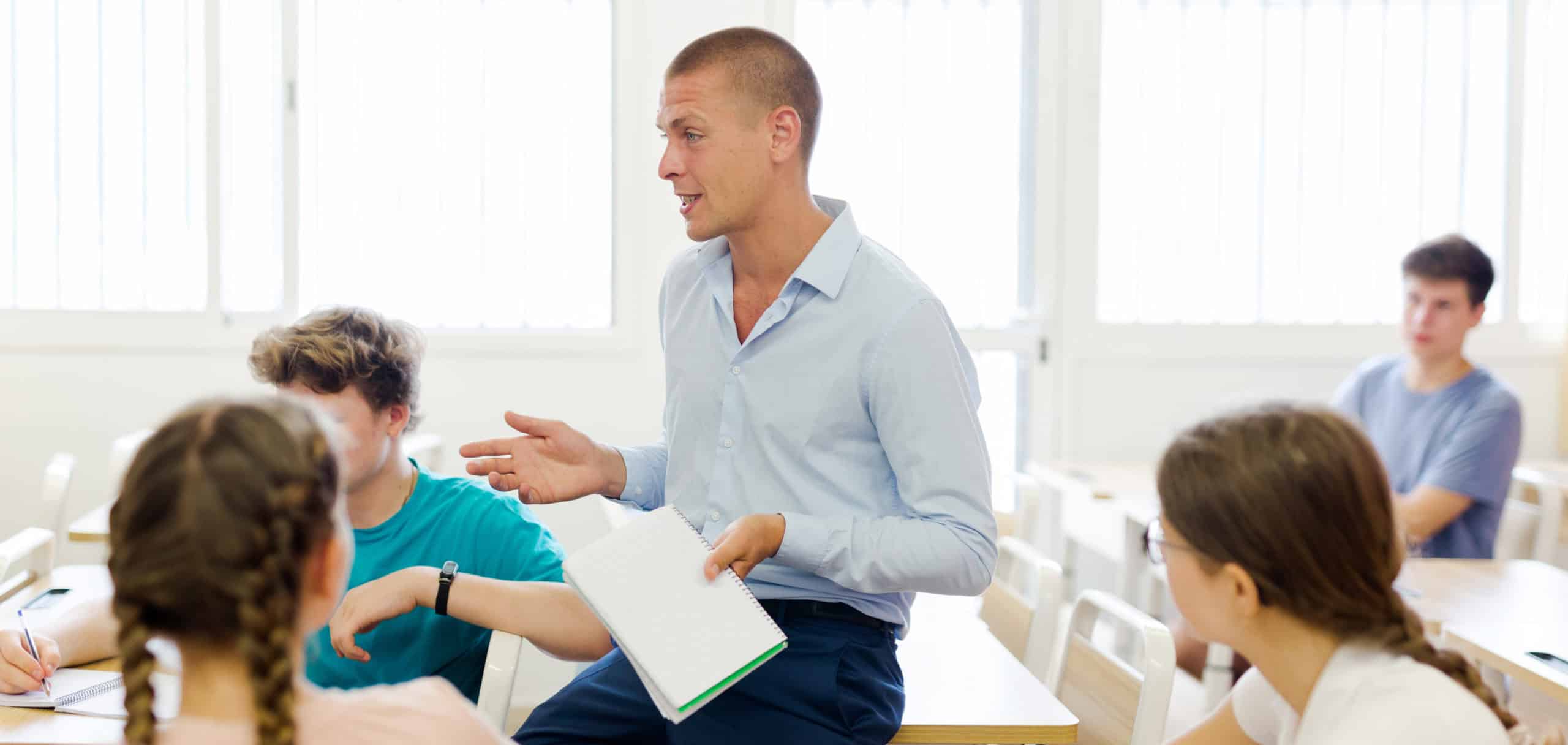 Friendly male teacher working with teen students in classroom at school