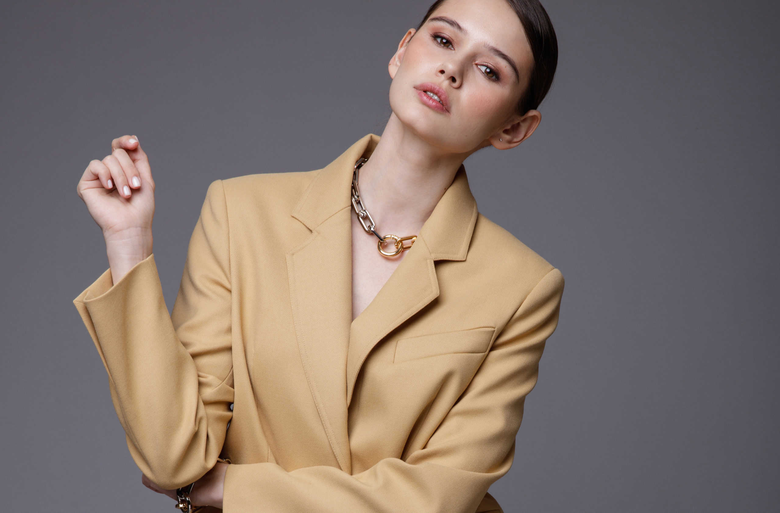 High fashion photo of a beautiful elegant young woman in a pretty  beige sand suit, jacket, pants, trousers, accessories posing on gray background. Studio Shot. Slim figure.