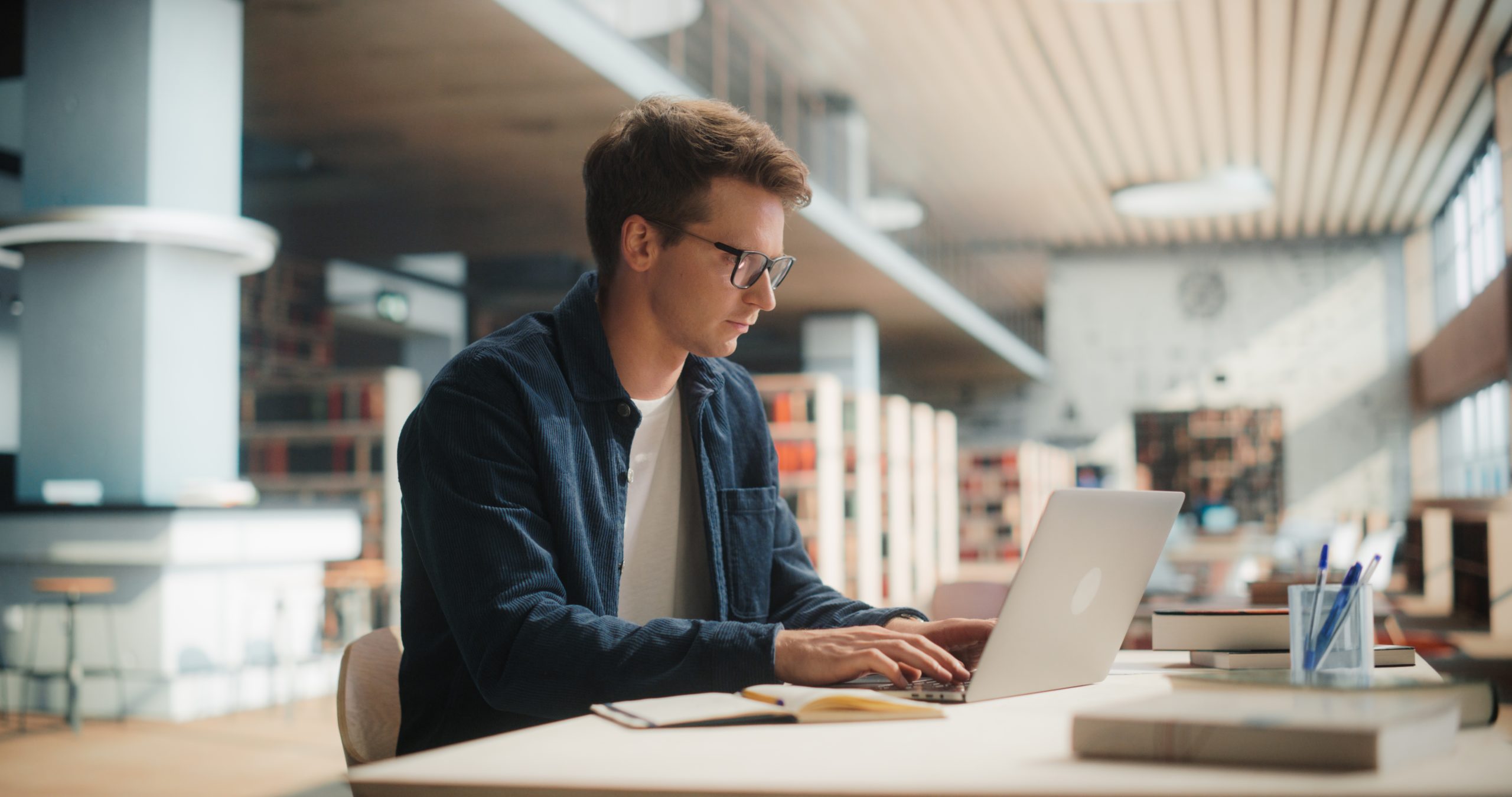 Young,Man,Studying,In,Modern,Library.,Caucasian,Male,Using,Laptop Young,Man,Studying,In,Modern,Library.,Caucasian,Male,Using,Laptop